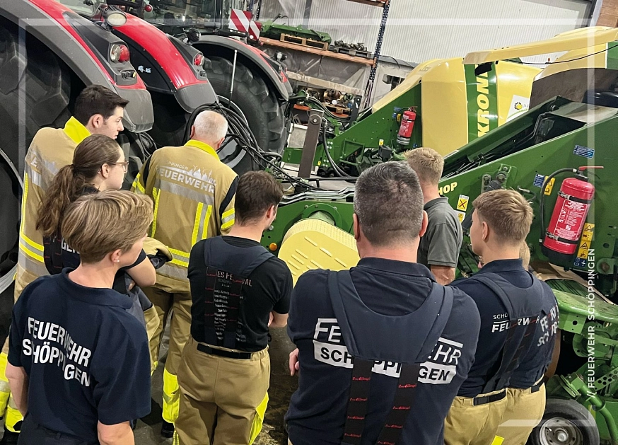 Mehrere Feuerwehrmänner stehen um einen roten Traktor mit Ballenpresse herum und schauen sich diesen genauer an.